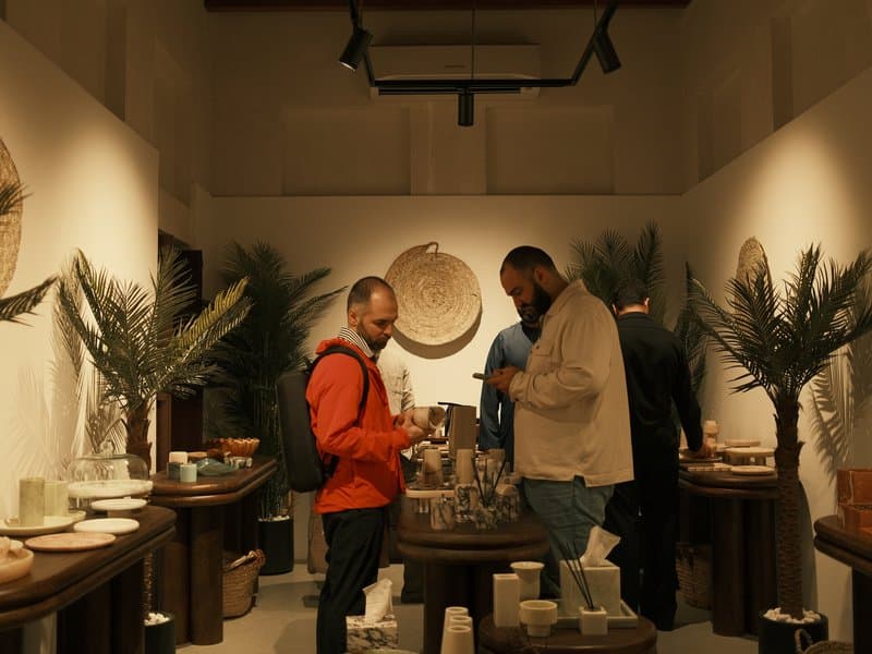 Two men interacting in a cozy indoor shop filled with decorative items and plants.