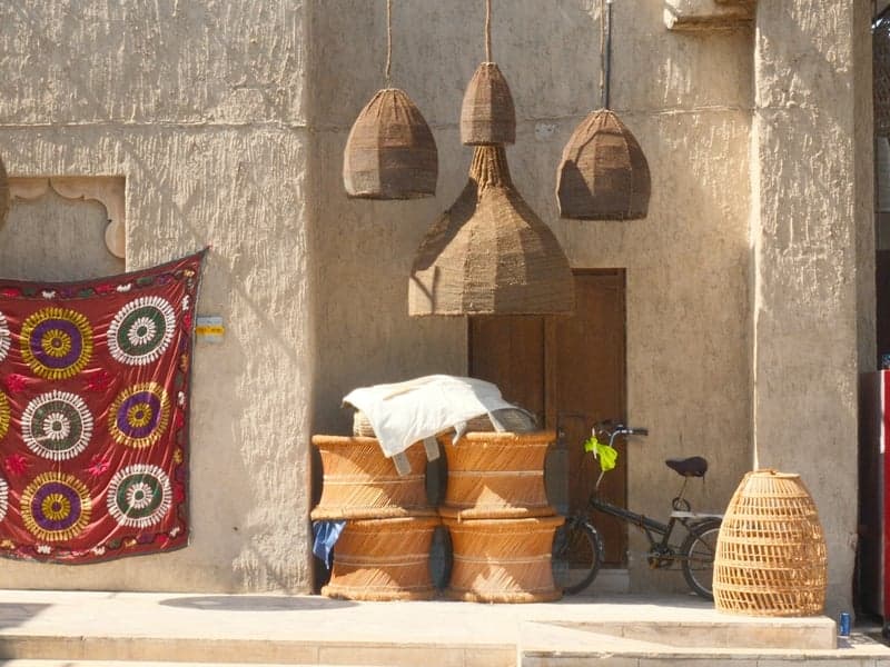 A rustic scene featuring woven baskets, a bicycle, and colorful textiles hanging on a wall.