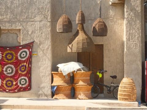 A rustic scene featuring woven baskets, a bicycle, and colorful textiles hanging on a wall.