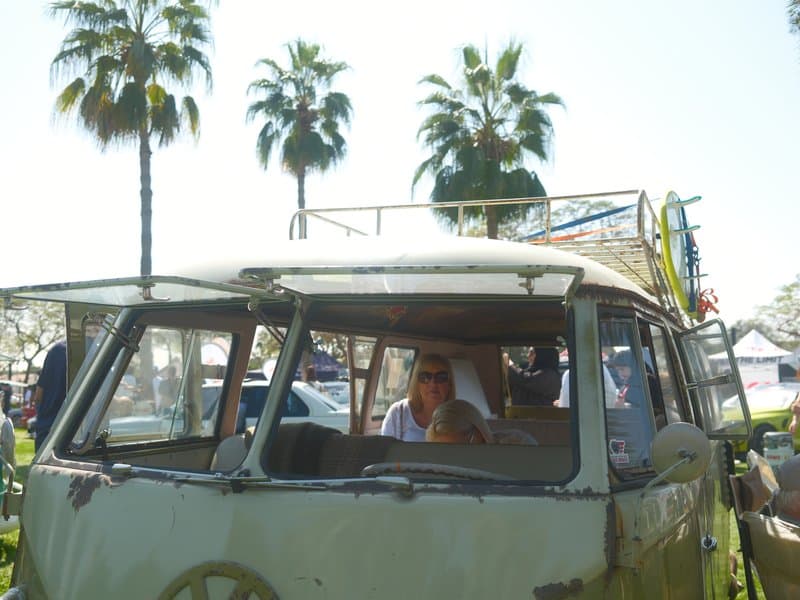 A vintage green Volkswagen van parked under palm trees with people inside, bright sunny day.