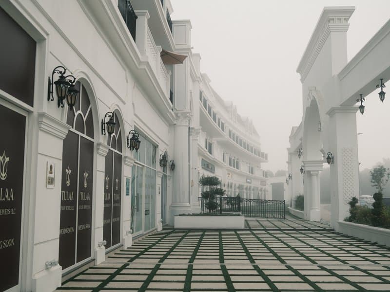 A foggy scene of a white architectural building with arched windows and a tiled pathway.