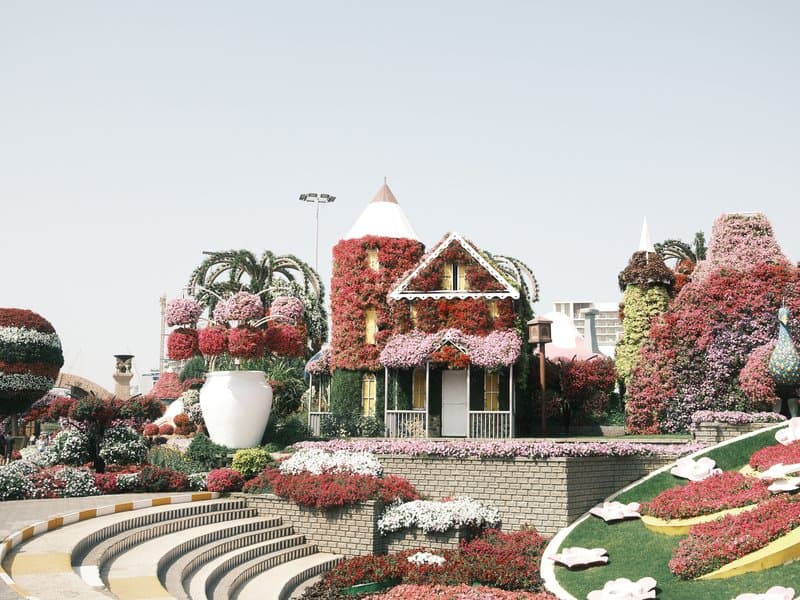 A colorful floral display featuring a whimsical house surrounded by vibrant flower arrangements.