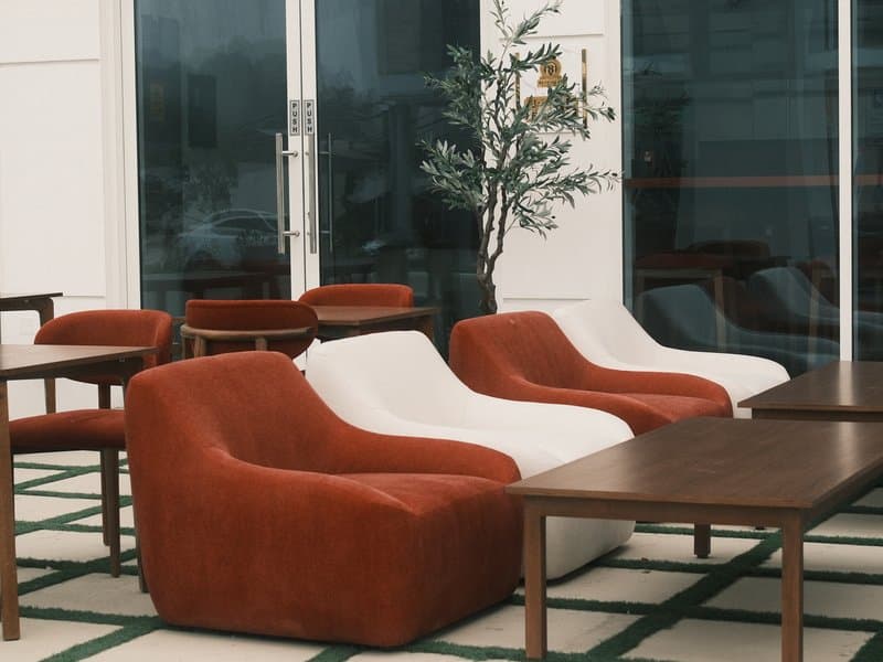 A modern indoor seating area with stylish chairs and wooden tables against a glass backdrop.