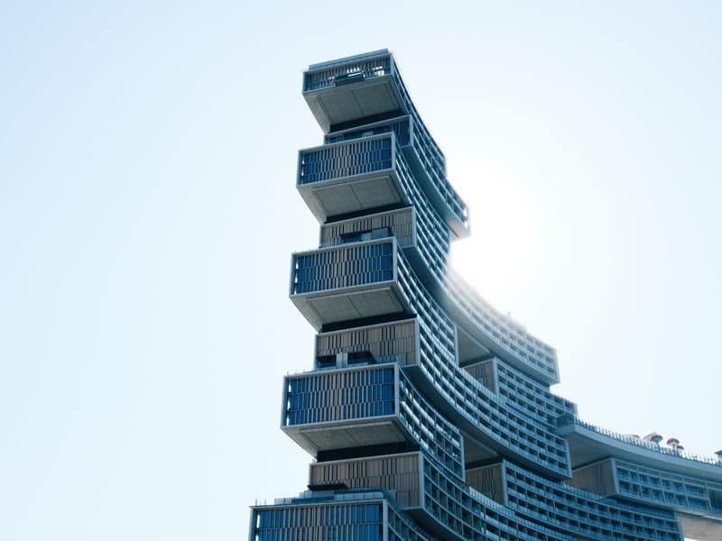 A modern architectural building with stacked balconies against a clear sky, sunlight glinting off the structure.