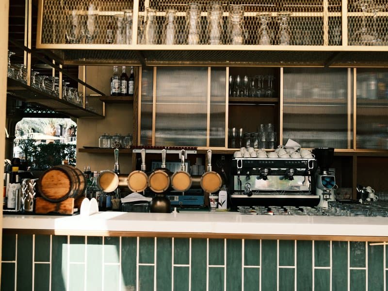 A stylish coffee bar with wooden barrels and glassware on display, featuring a modern espresso machine.