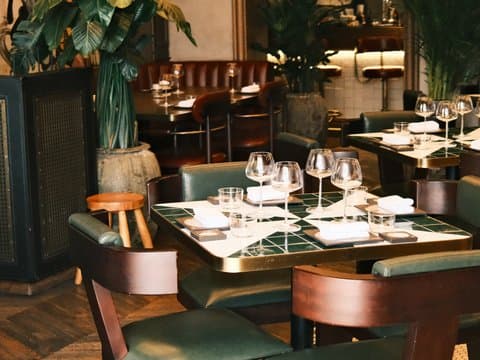 Elegant restaurant interior with tables set for dining, featuring green chairs and glassware.