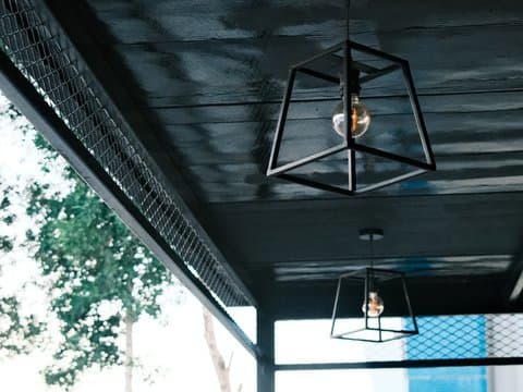 Interior view of modern pendant lights hanging from a ceiling with a dark finish and greenery visible outside.