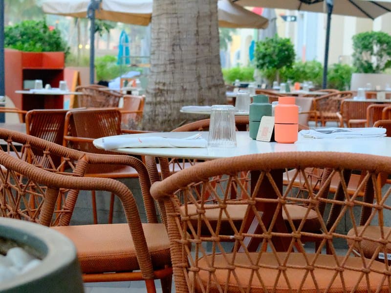 A cozy outdoor dining area with woven chairs and tables surrounded by greenery.