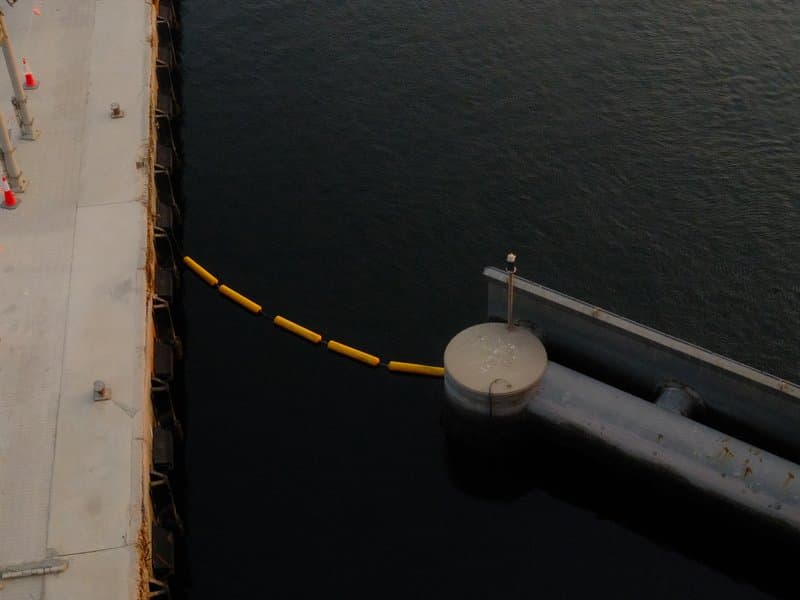 Aerial view of a circular dock extending into dark water, with a yellow barrier floating nearby.
