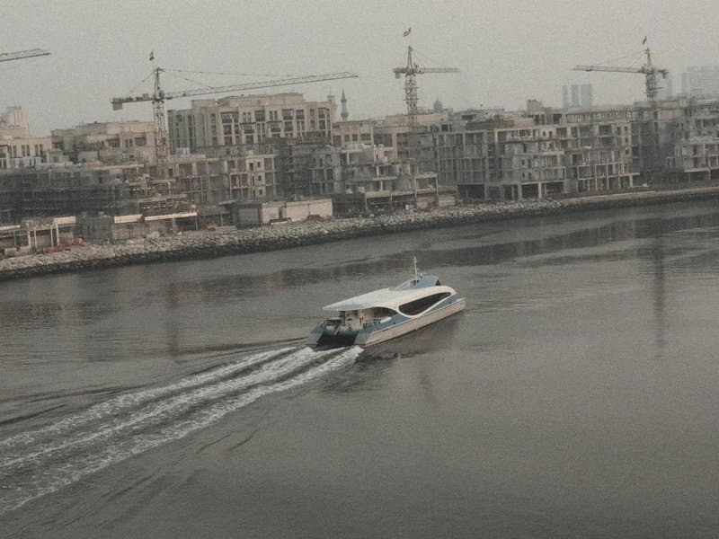 A boat gliding through calm waters with construction cranes and buildings in the background.