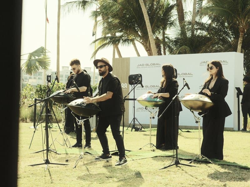 A group of musicians performing with steel drums outdoors, surrounded by palm trees.