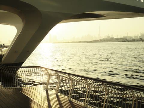 A view of a waterfront with a curved railing and soft sunlight reflecting on the water.