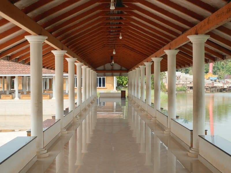 A corridor with columns leading to a serene water view, featuring wooden beams and polished floors.
