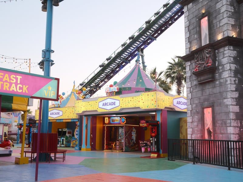 Colorful amusement park entrance with a roller coaster overhead and vibrant decorations.