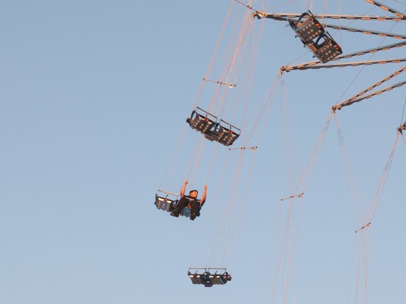 People enjoying a swing ride at an amusement park against a clear blue sky.