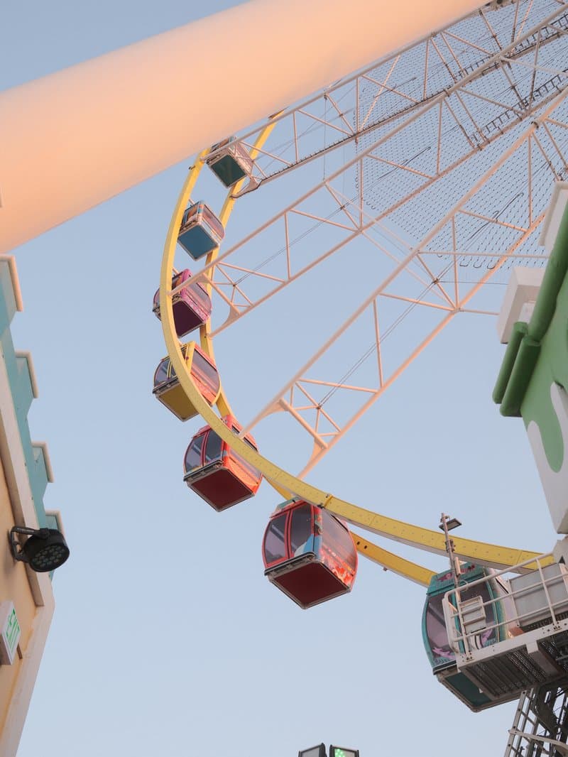 Colorful ferris wheel gondolas against a clear sky during sunset.