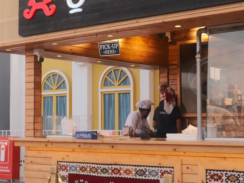 Two chefs working at a food stall with a wooden counter and colorful background.