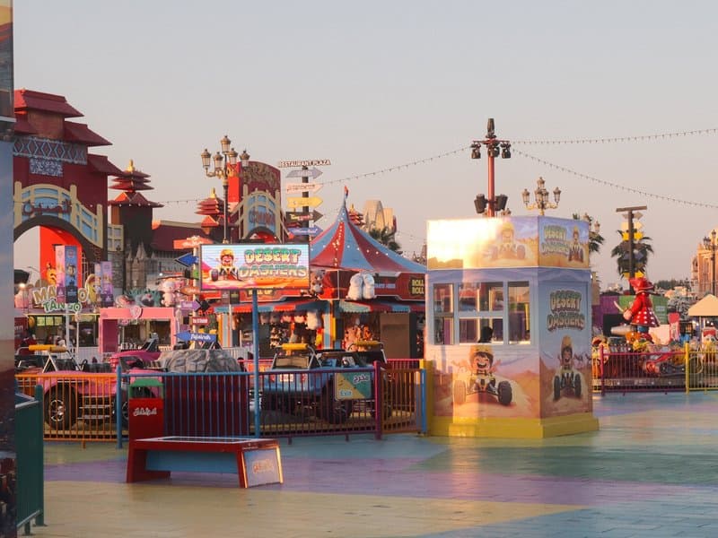 Colorful carnival scene with rides and booths under a pastel sky at sunset.