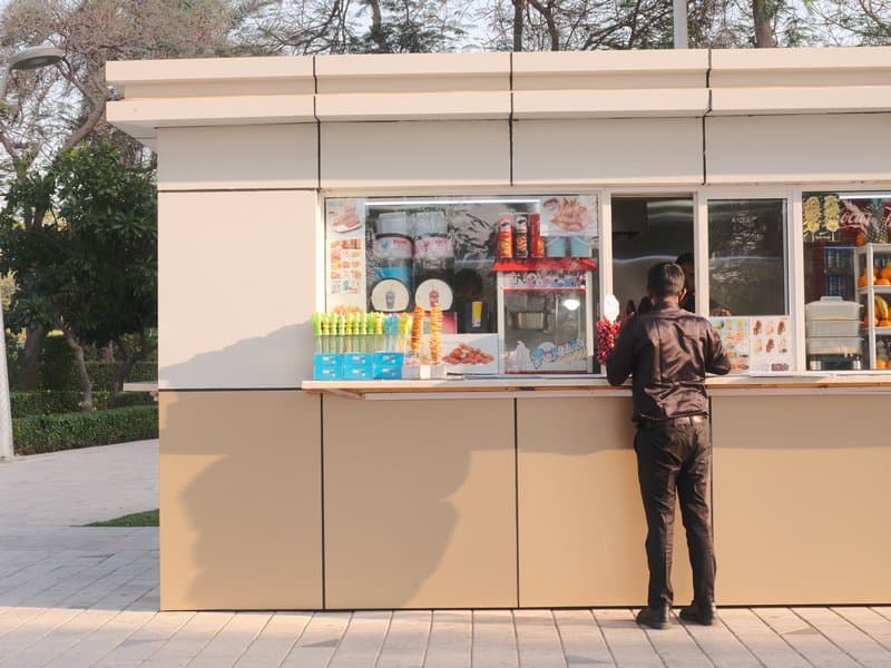 A person in a black jacket ordering at an outdoor kiosk with colorful signage.