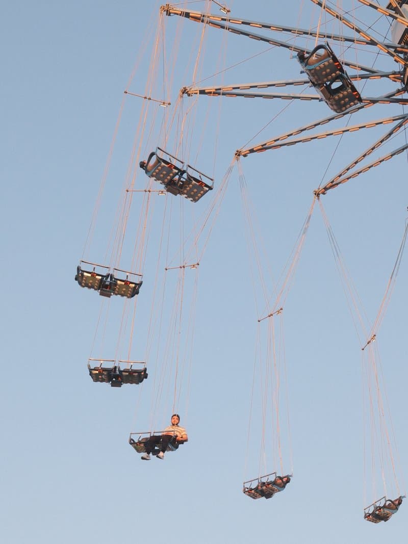 A swing ride at an amusement park with several seats suspended in the air against a clear blue sky.