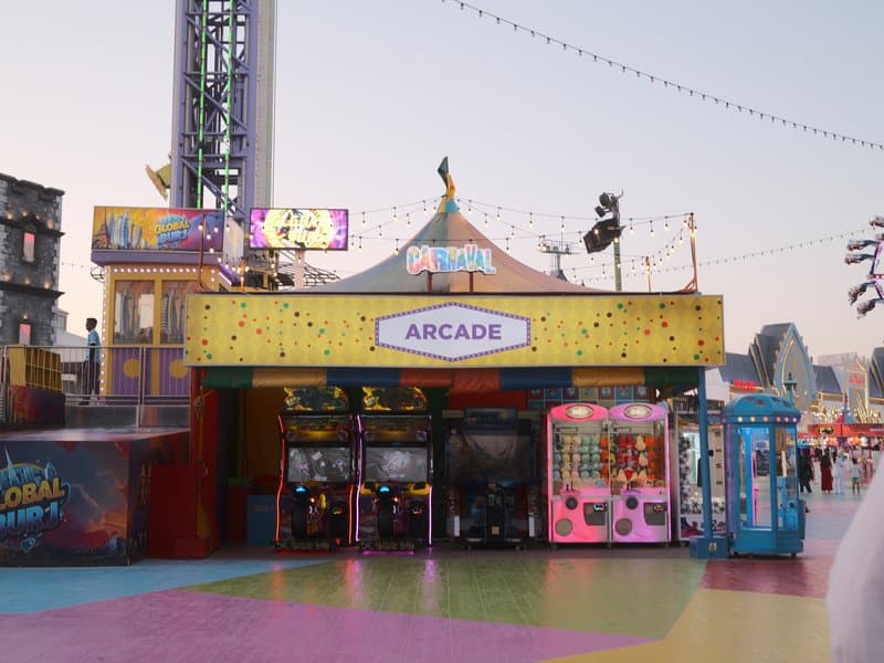 Colorful arcade entrance with games and bright lights at a fairground during twilight.