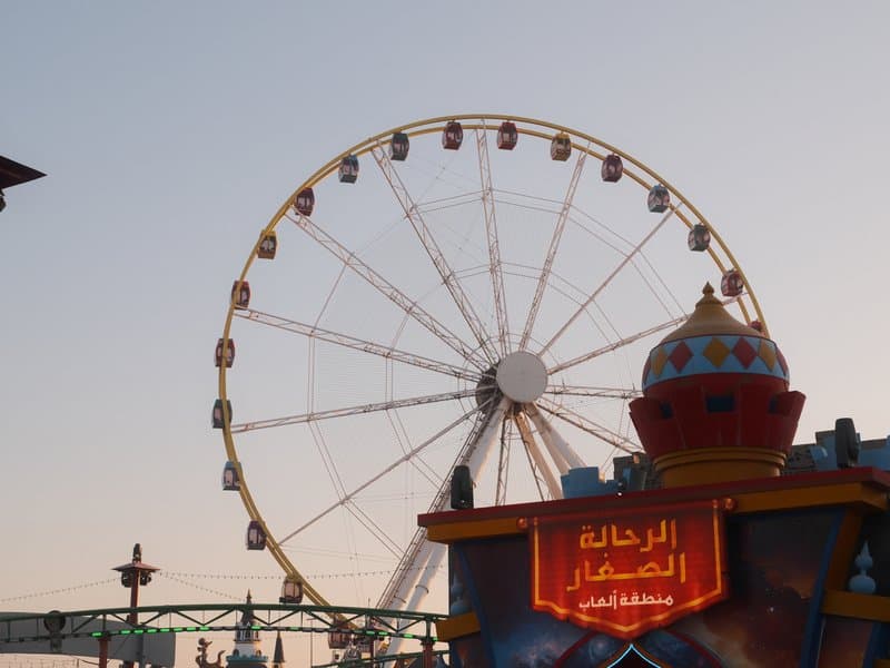 Ferris wheel against a sunset sky with a colorful structure in the foreground.