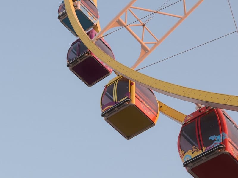 Colorful ferris wheel gondolas against a clear sky.