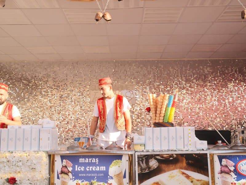 Two ice cream vendors in traditional attire serving ice cream at a festive event with colorful decorations.