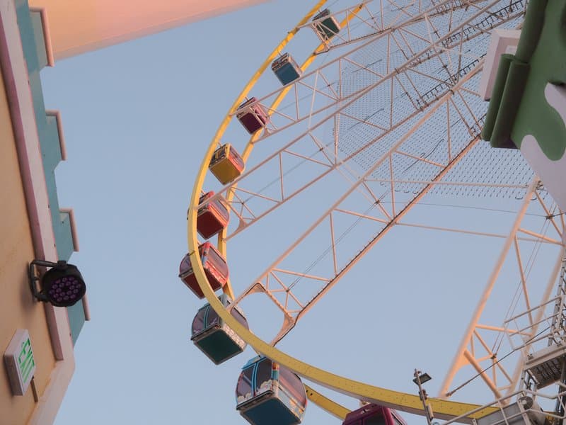 A colorful ferris wheel against a clear sky, viewed from below with buildings on either side.
