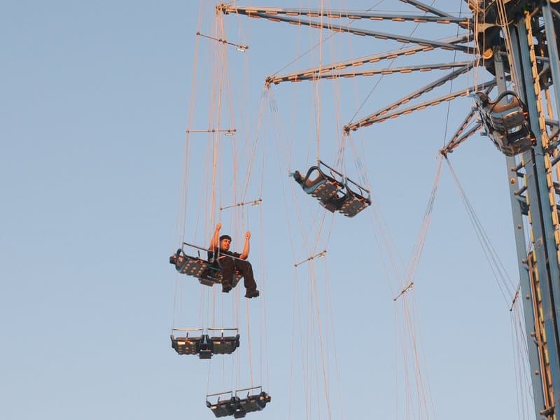 A person sitting on a swing ride at an amusement park against a clear blue sky.