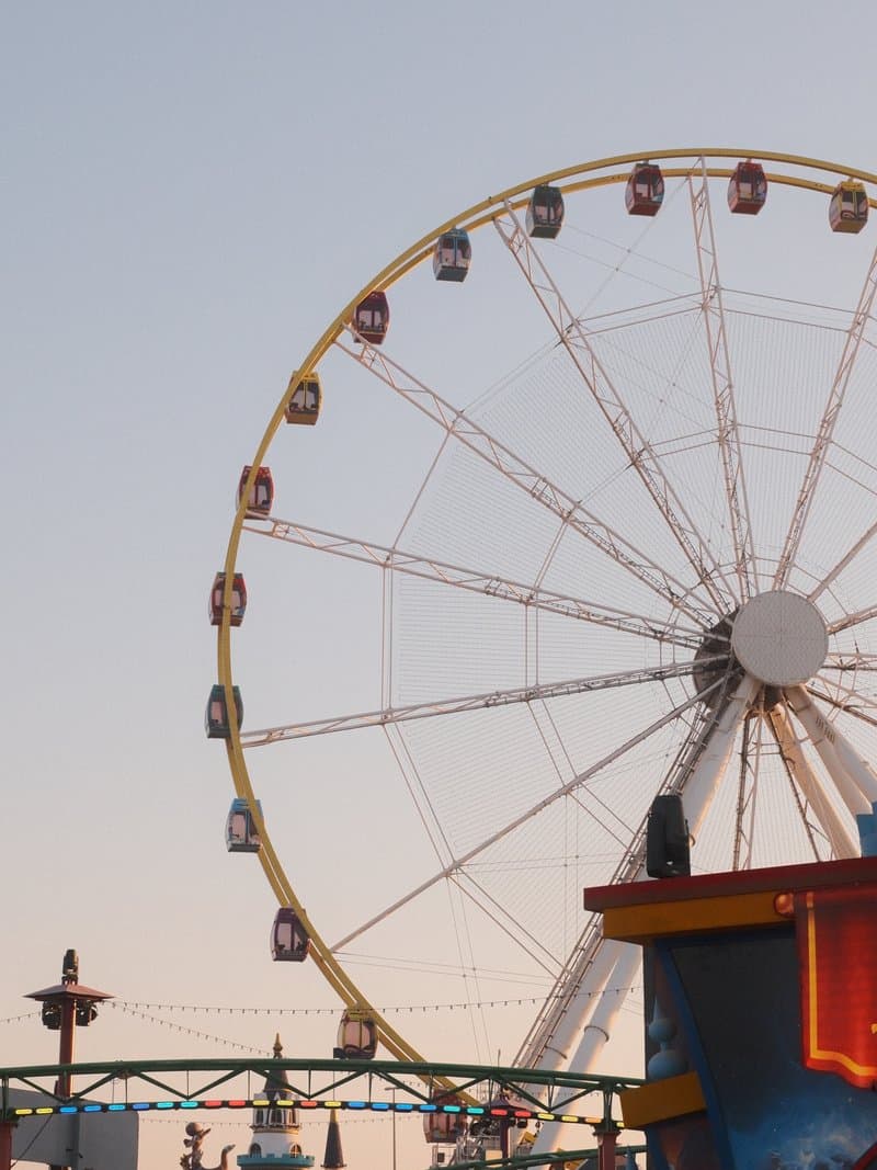 A ferris wheel against a pastel sky during sunset, with colorful gondolas and a vibrant amusement park setting.