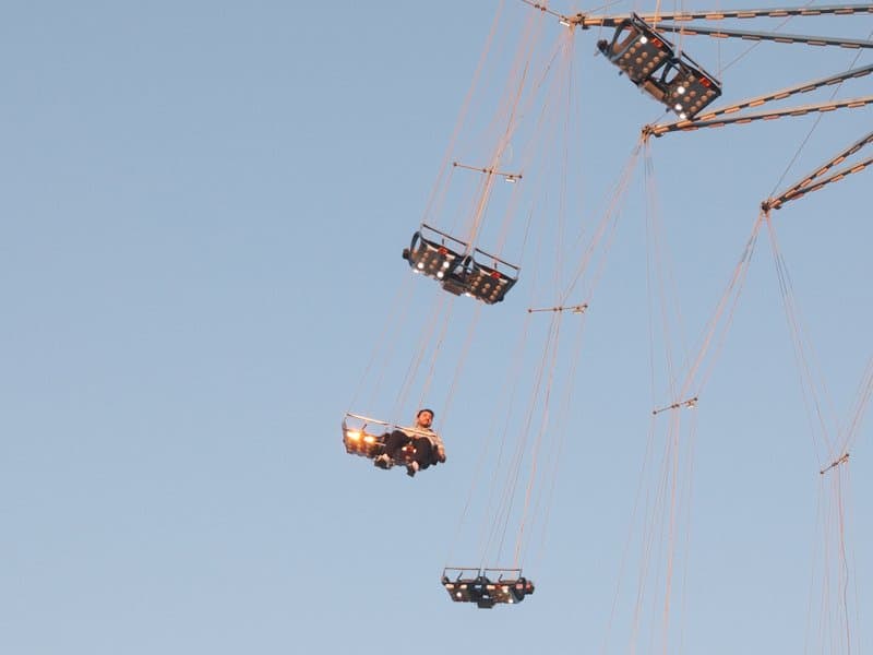 A person enjoying a swing ride at an amusement park against a clear blue sky.