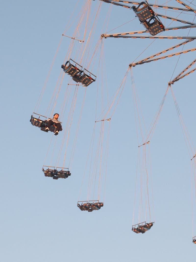 A child enjoying a swing ride at a fair, suspended high against a clear blue sky.