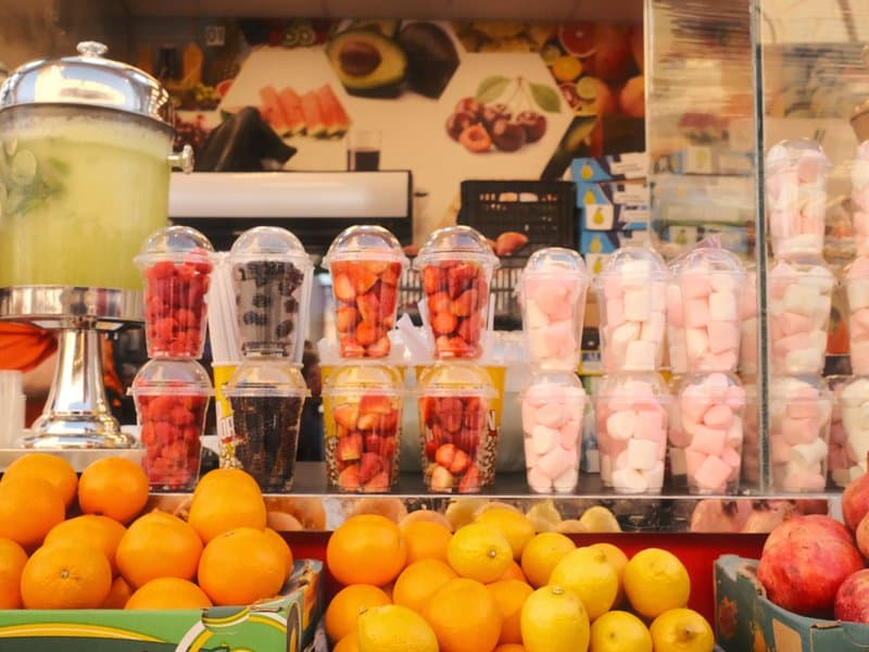 Colorful display of fruit cups and candies at a market stall with oranges and pears in the foreground.