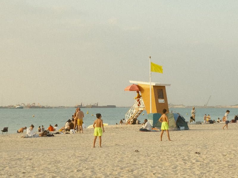 A beach scene with a lifeguard tower, children playing, and people relaxing on the sand.