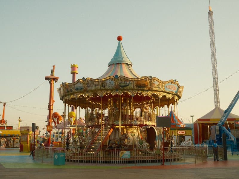 A vintage carousel at an amusement park during golden hour, with colorful decorations and a clear sky.