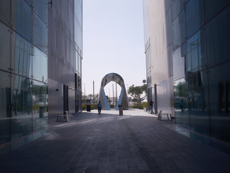 A modern archway between two glass buildings in an urban setting under clear skies.