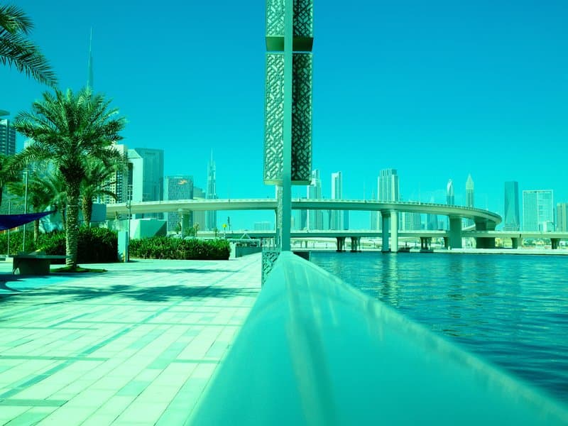 A vibrant urban waterfront scene featuring a modern bridge and skyscrapers under a turquoise sky.