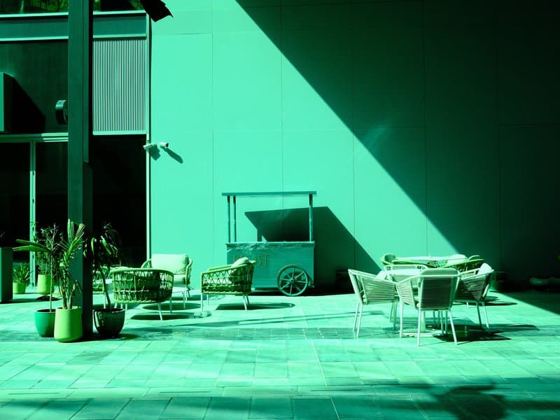 A modern outdoor seating area with green walls and geometric shadows, featuring chairs and a table.