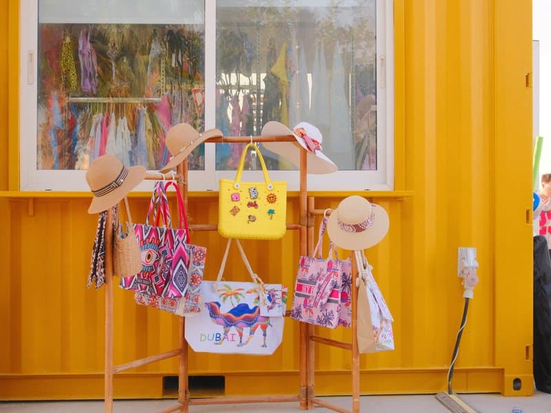Colorful display of hats and bags in front of a bright yellow wall.
