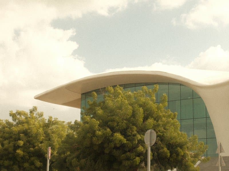 Modern building with a curved roof surrounded by trees under a cloudy sky.
