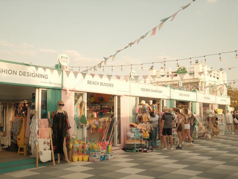 A vibrant beach market scene with colorful stalls and people browsing in warm evening light.