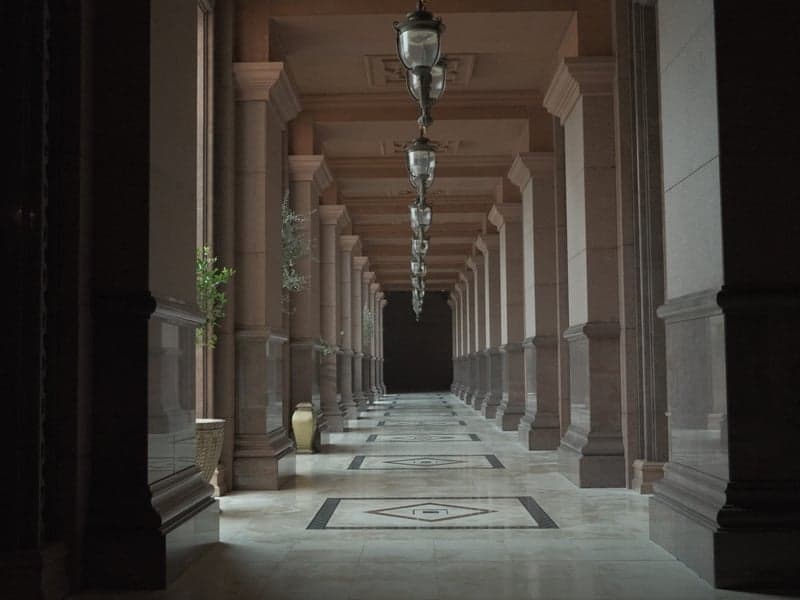A long corridor with columns and decorative lighting, leading to a dark end.