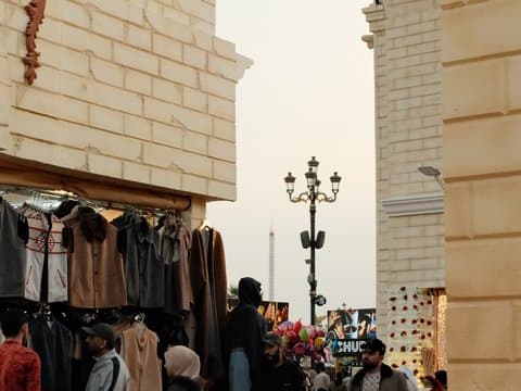 A bustling market scene with clothing stalls and people shopping under a soft evening light.