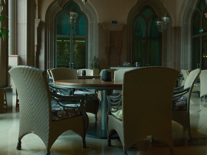 A cozy indoor seating area with elegant chairs and a round table, surrounded by arched windows.
