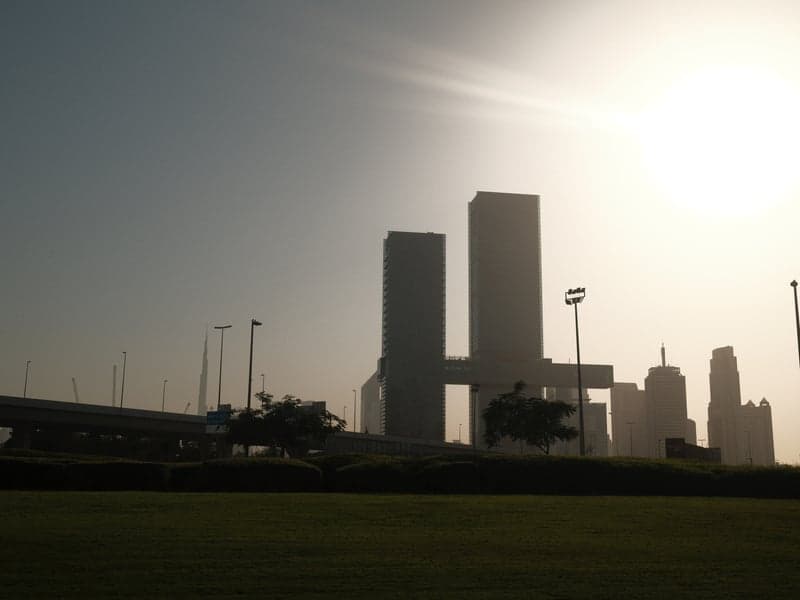 Silhouetted skyscrapers against a bright sky, with a hazy urban landscape in the background.