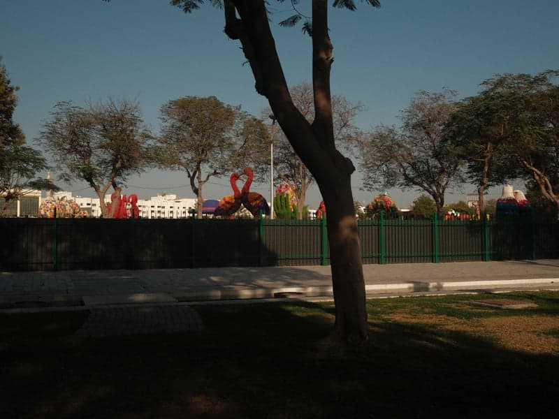 A park scene featuring a large red sculpture, trees, and a clear blue sky.