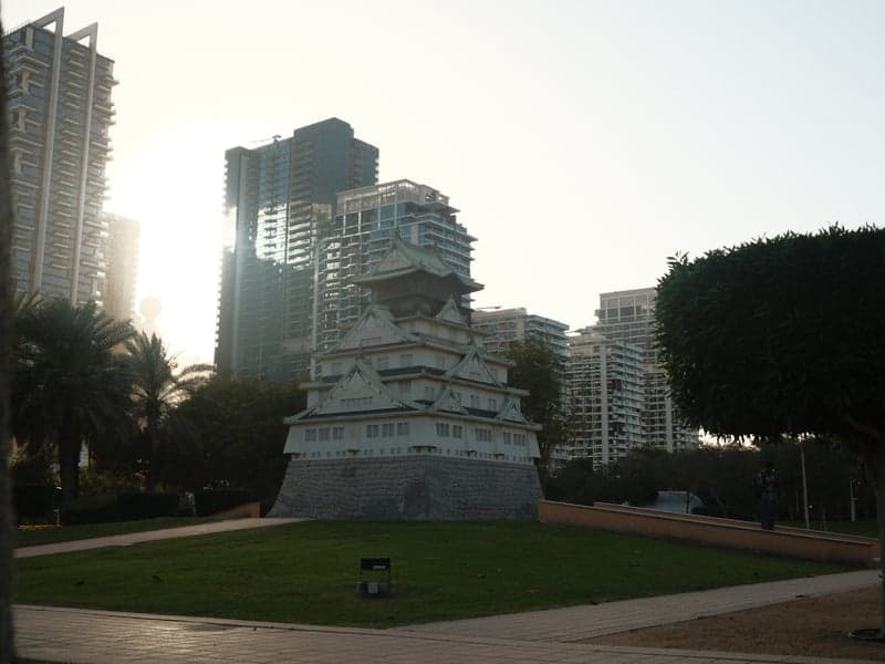 A monument surrounded by modern buildings and palm trees during golden hour.