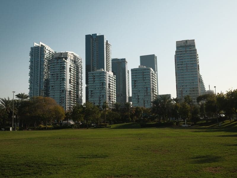A view of modern skyscrapers against a clear blue sky, with a green park in the foreground.