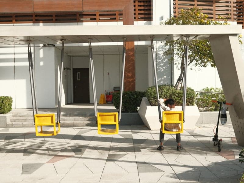 A child sitting on a yellow swing in a modern urban setting with a minimalist design.